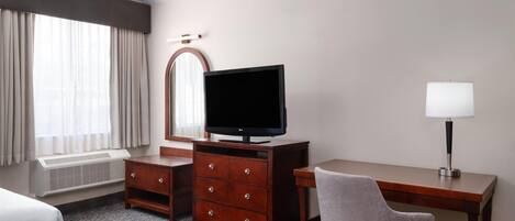 A hotel room with a bed, a desk with a chair, a television, a lamp, and a mirror.