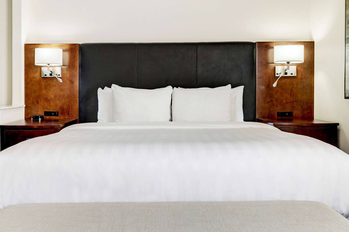 A hotel room with a large bed, two nightstands, and wall-mounted lamps.