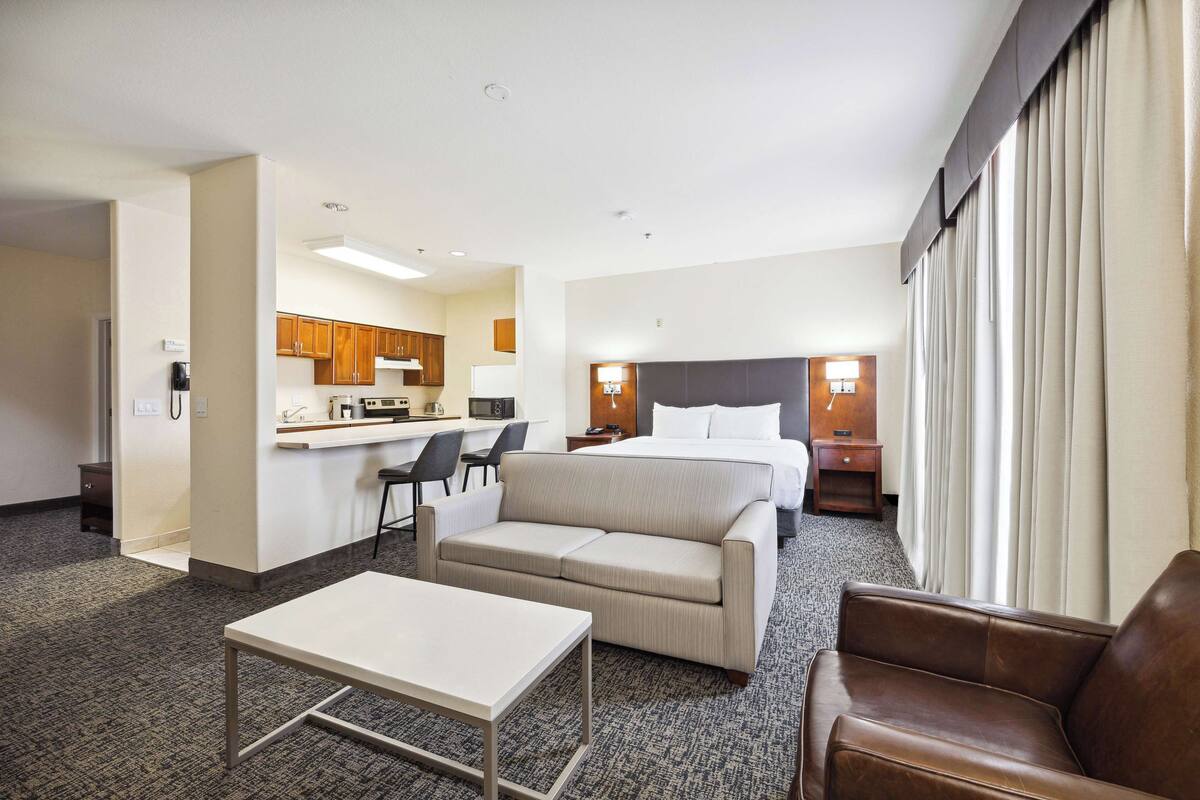 A hotel room with a kitchenette, a bed, a sofa, a table, and a chair.