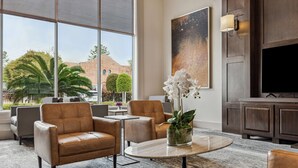 Una hall moderna con poltrone in pelle, un tavolino con un vaso di fiori, un quadro di grandi dimensioni e un televisore su un mobile in legno.