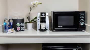 Un comptoir de cuisine avec un four à micro-ondes, une machine à café, une orchidée en pot et des bouteilles d’eau.