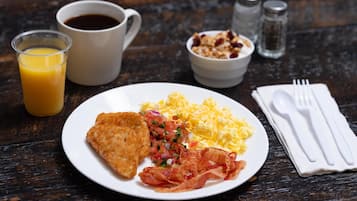Ein Teller mit Rührei, Speck und einer gebratenen Speise, dazu ein Glas Orangensaft und eine Tasse Kaffee.
