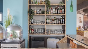Una zona de bar con mostrador de madera, estantes con botellas y un refrigerador.