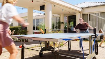 Una instalación de tenis de mesa al aire libre con una mesa y red portátiles, ubicada en un espacio exterior cubierto con un edificio al fondo.