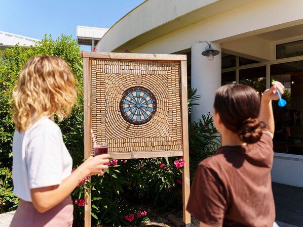 Un dardo colgado en una estructura de madera con un diseño circular, situado al aire libre con vegetación y un edificio al fondo.