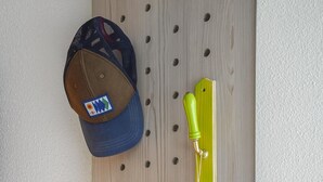 Una pared de tablero de madera con varios objetos, como una gorra, un gancho amarillo y una bolsa de tela blanca.