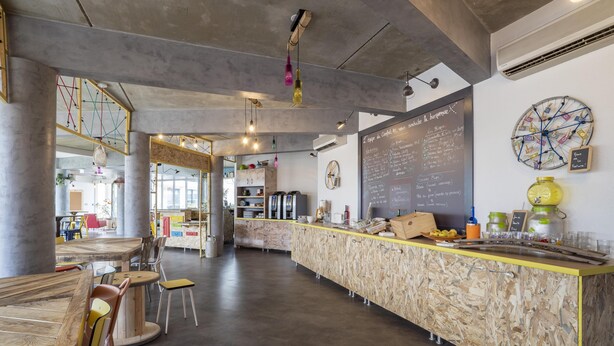 Interior moderno de una cafetería con mostrador de madera, zona de estar y un menú en la pizarra.