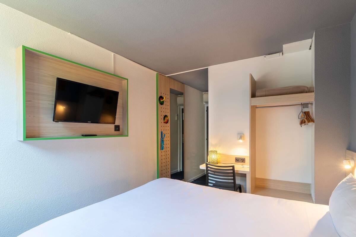 Habitación de hotel con cama, televisión en la pared, escritorio con silla y armario.