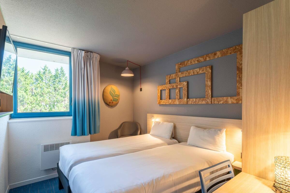 Une chambre d’hôtel avec deux lits, un bureau, une chaise, une fenêtre avec des rideaux, une horloge murale et un panneau décoratif en bois.