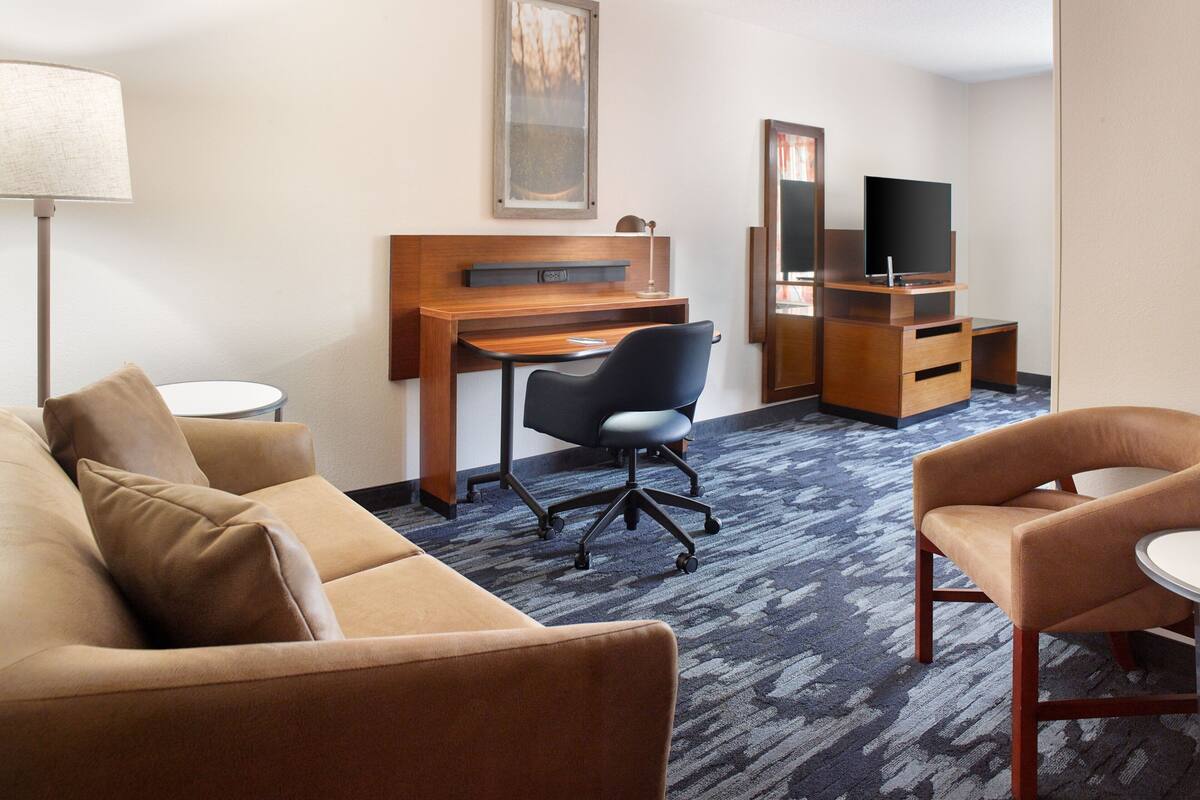 Una habitación de hotel con sofá, escritorio, silla, televisor y espejo.
