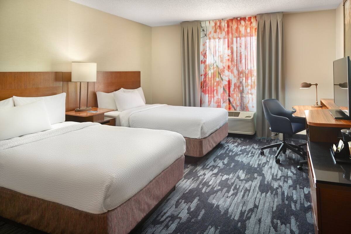 Una habitación de hotel con dos camas, un escritorio con computadora y televisión.