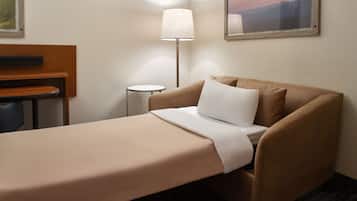 A single bed with a beige bedspread and pillows, a bedside table, a lamp, and a framed picture on the wall.