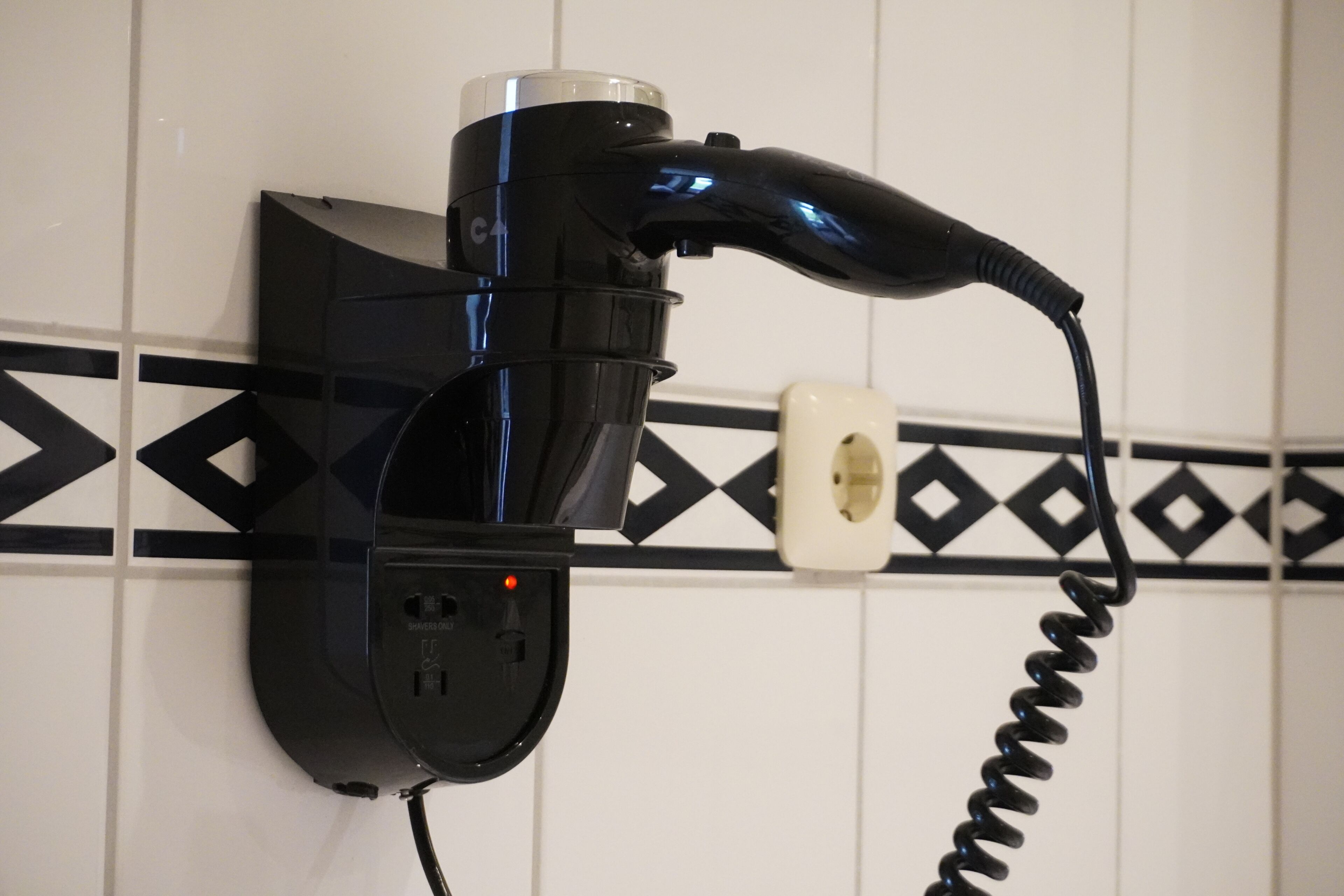 A hairdryer mounted on a wall with a power outlet and a coiled cord.