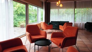 A room with large windows, orange chairs, a black table, and a green sofa. - Westlake Hotels Amsterdam (Amsterdam)