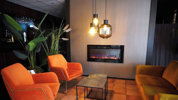 A bar area with orange chairs, a small table, and a flat-screen TV mounted on the wall. - Westlake Hotels Amsterdam (Amsterdam)