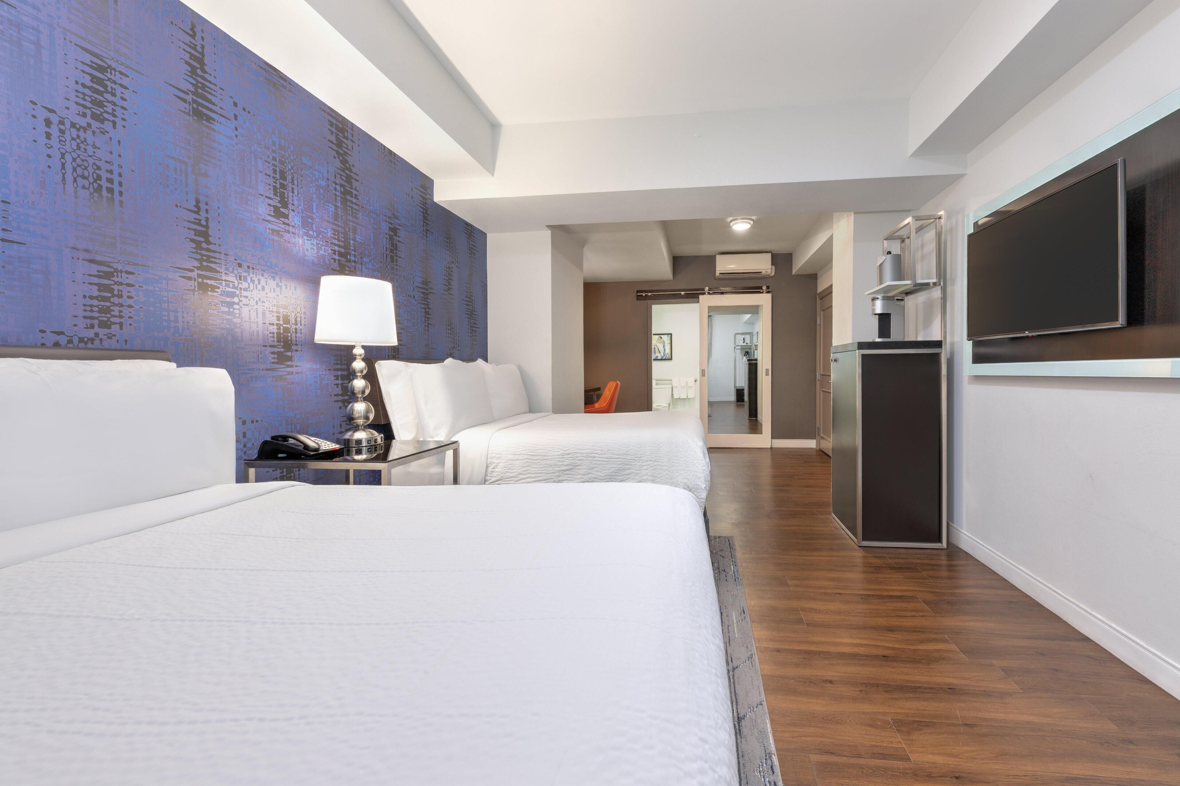 A hotel room with two beds, a desk with a lamp, a TV, and a wardrobe.