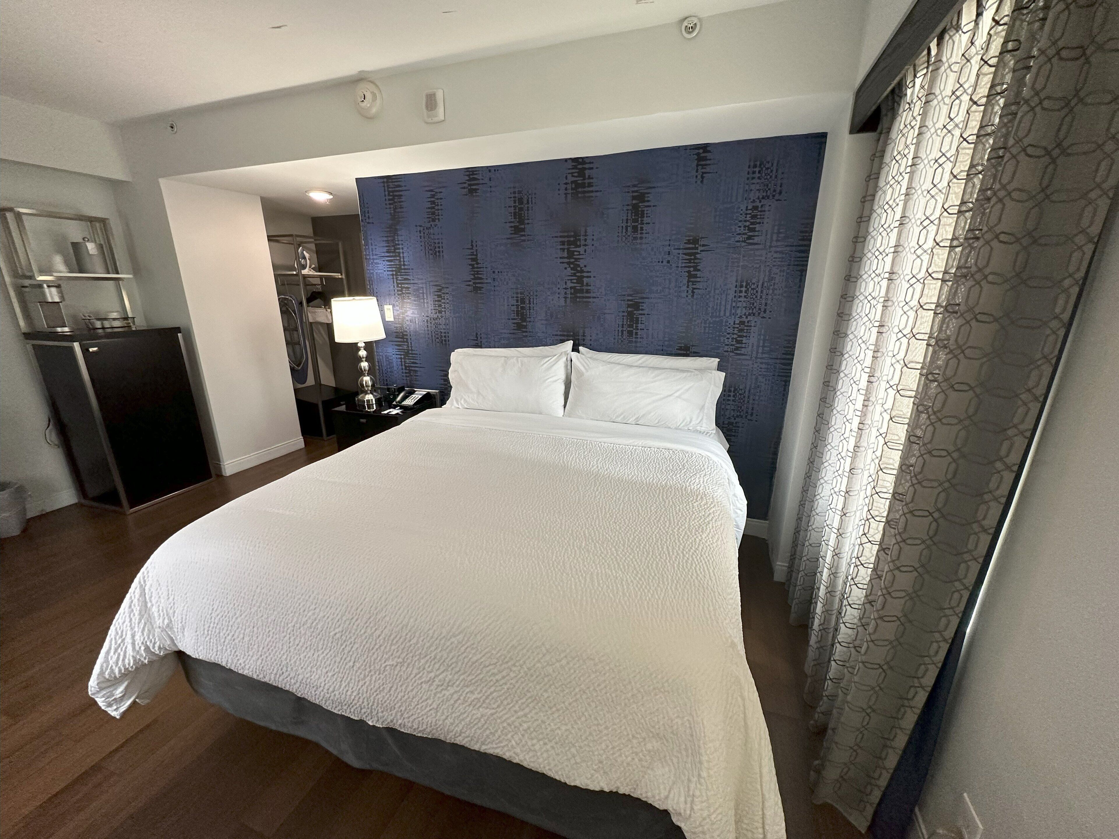 A hotel room with a large bed, a desk, a lamp, and a wardrobe.