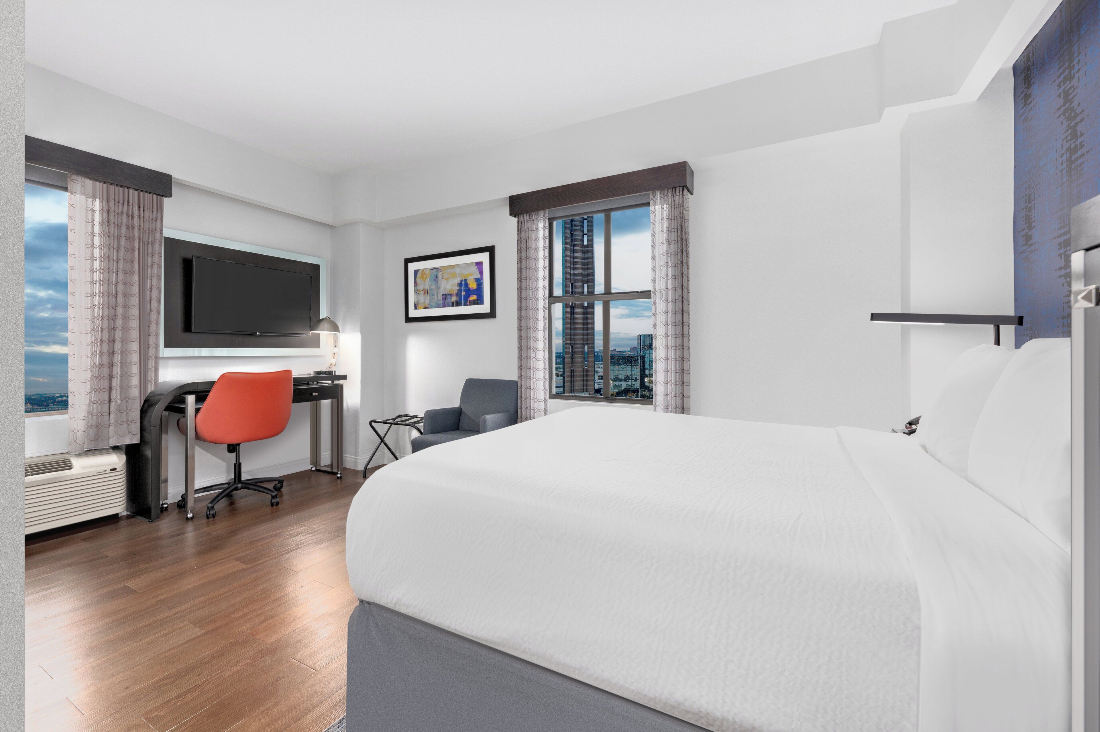 A hotel room with a large bed, a desk with a chair, a television, and a window with curtains.