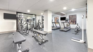 Un gimnasio con cintas de correr, elípticas y un banco.