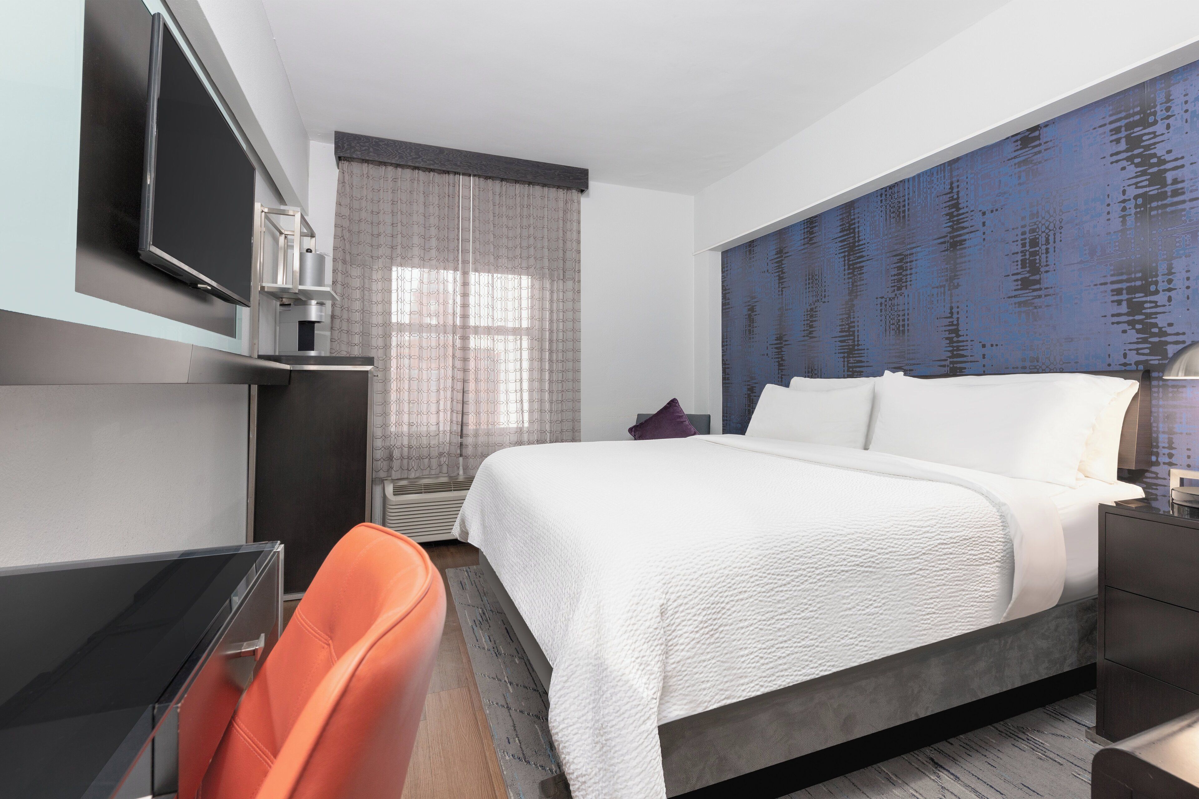 Una habitación de hotel con una cama grande, televisión, escritorio y una silla.