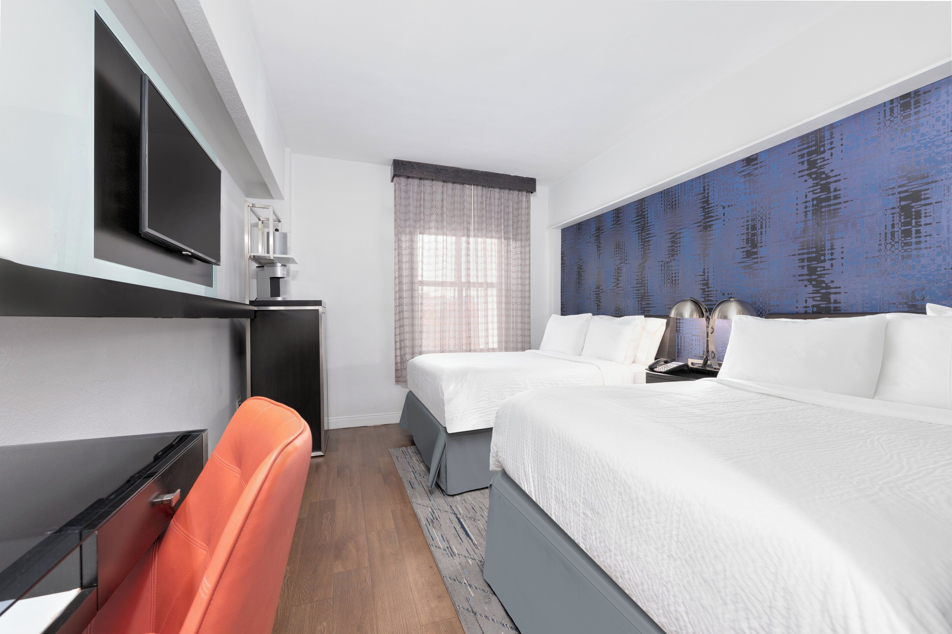 Ett hotellrum med en säng, ett skrivbord, en stol, en tv och ett fönster med gardiner.