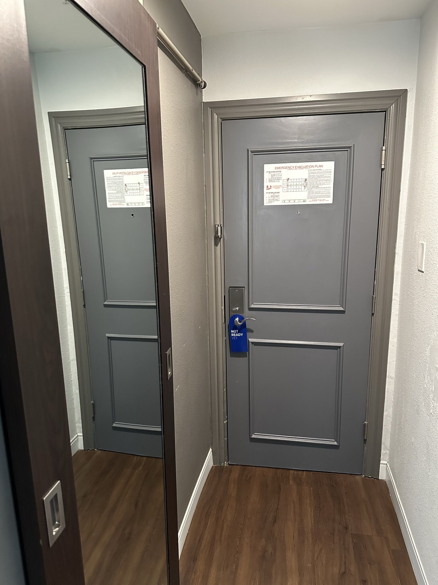 A closed door with a blue "Not Ready" sign, a mirror reflecting the door, and a wooden floor.