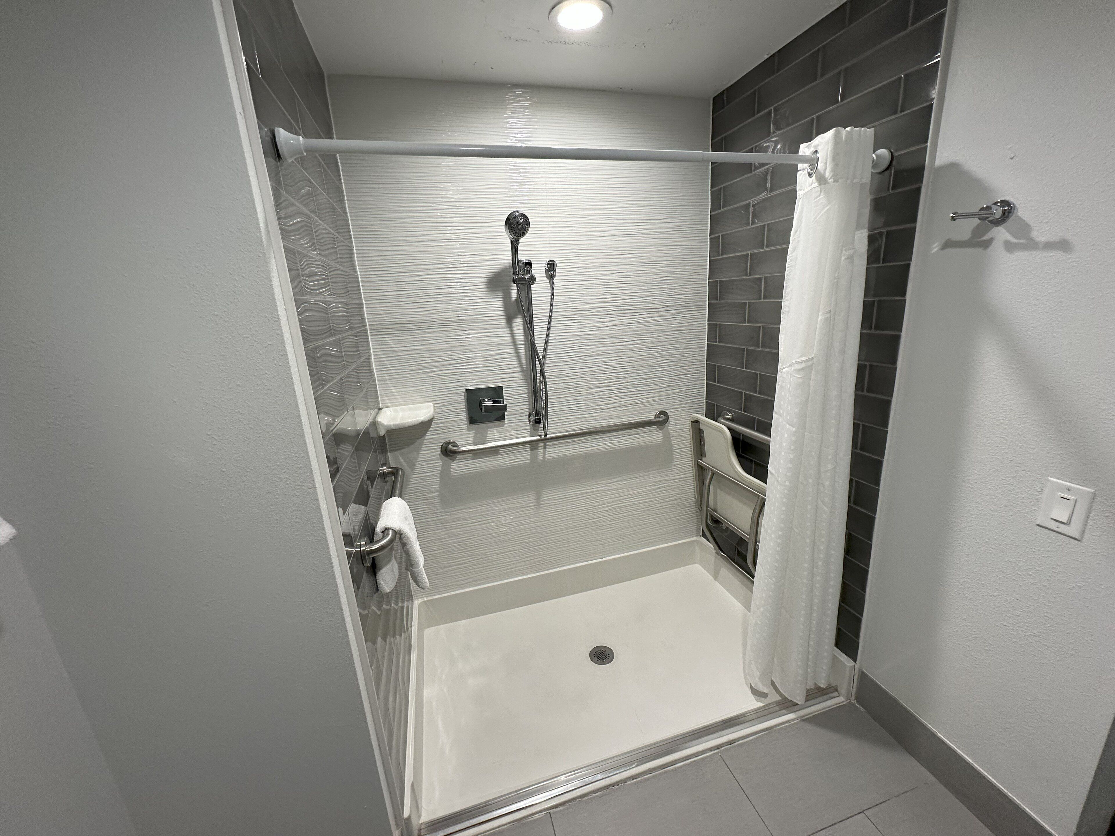 A wheelchair-accessible shower with a handrail, a grab bar, and a white curtain.
