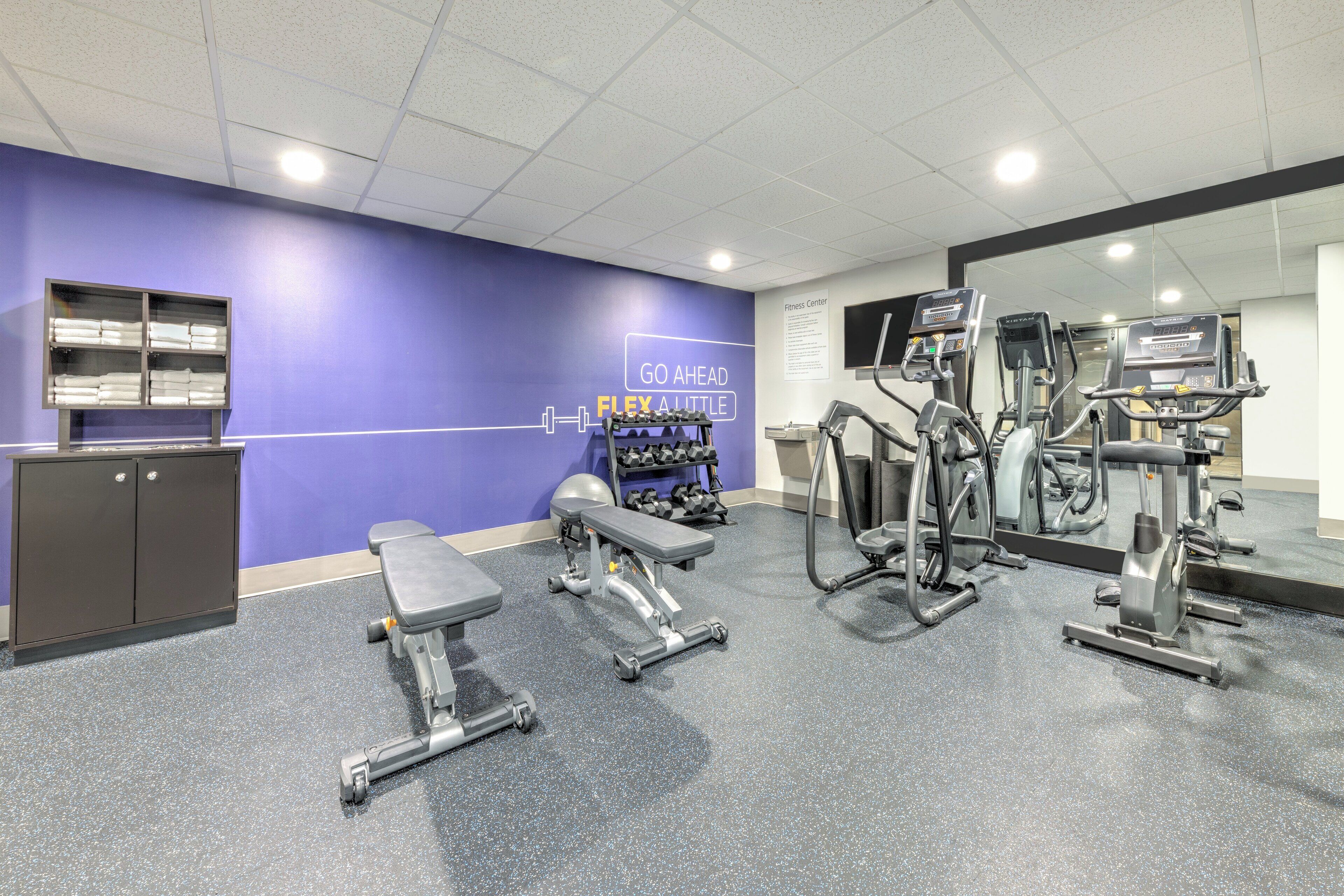A gym with exercise equipment, a bench, and a wall with a motivational sign.