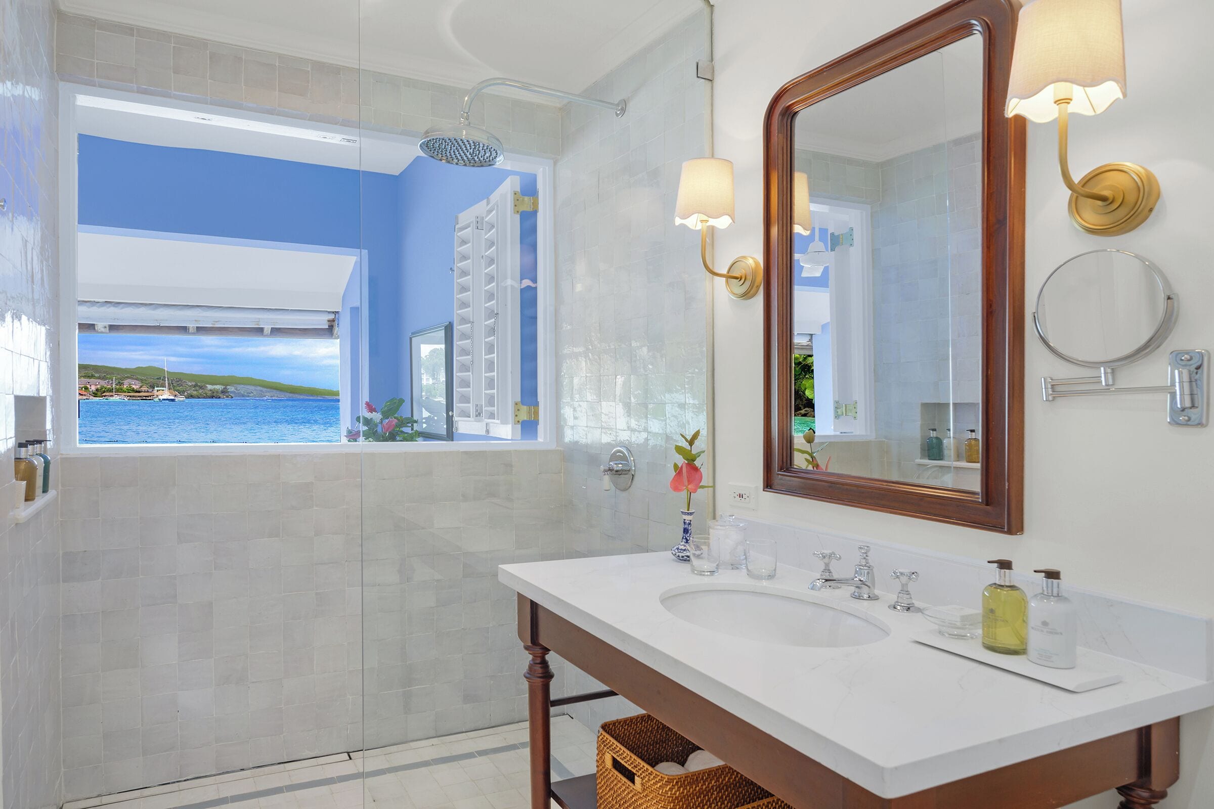 A bathroom with a large mirror, two sinks, and a view of the sea through a window.