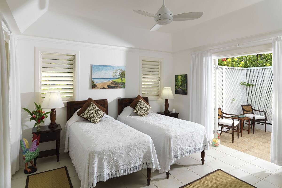 A room with two beds, a ceiling fan, a dining area with chairs, and a view of the outdoors.