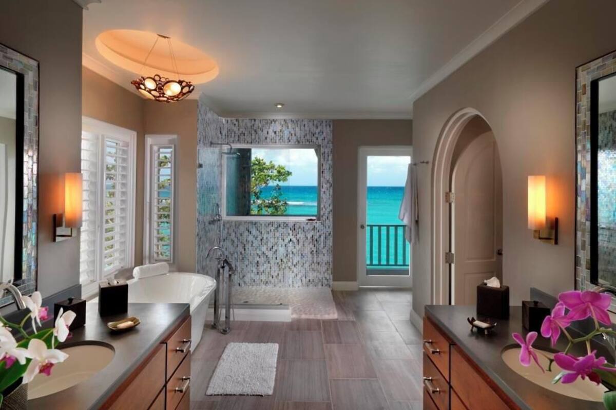 A bathroom with a view of the ocean, a bathtub, a shower, and a vanity with a sink and mirror.