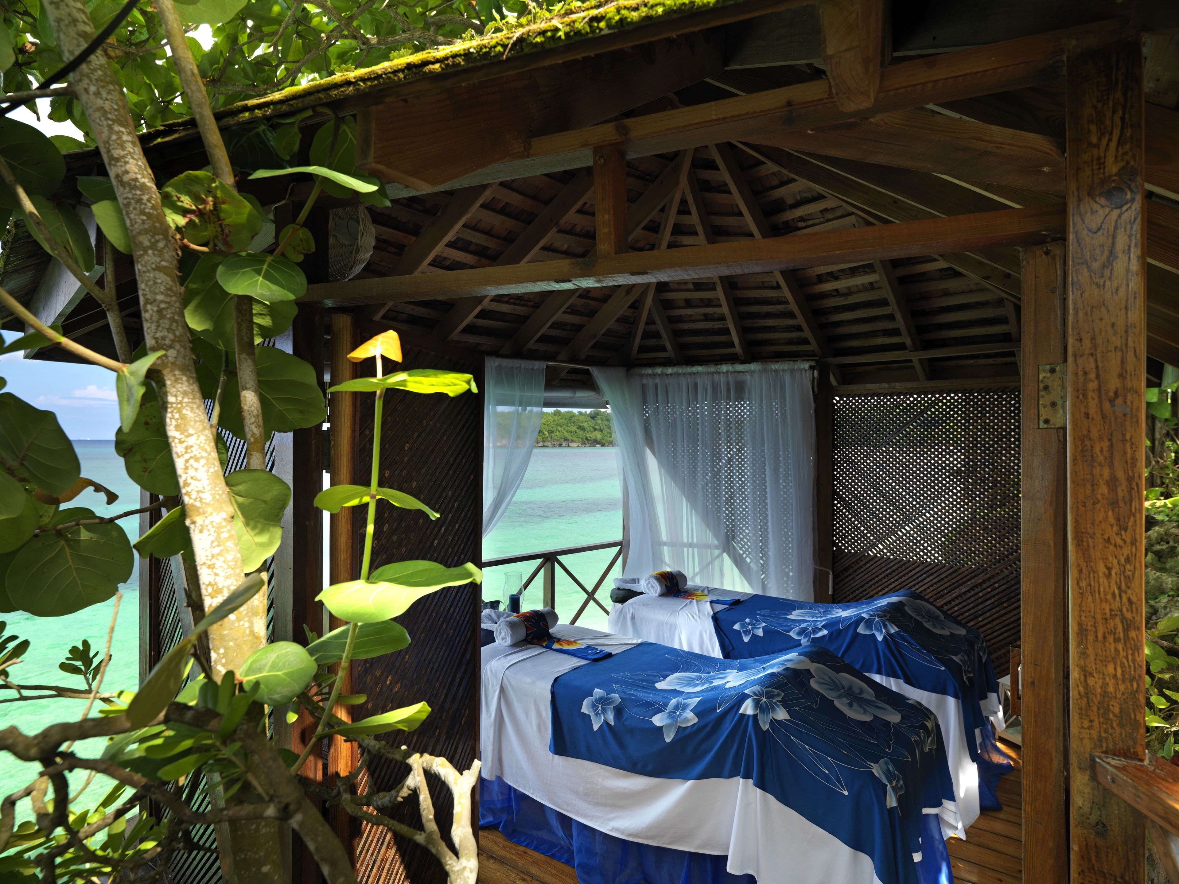 A wooden room with a bed, a window with a view of the ocean, and a hanging plant.