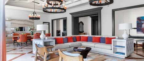 A spacious living room with a large sectional sofa, a dining area with orange chairs, and a chandelier.