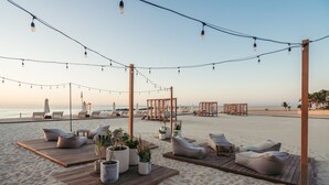 A beachside lounge area with wooden deck seating, potted plants, and string lights. - Hilton Los Cabos (San José del Cabo)
