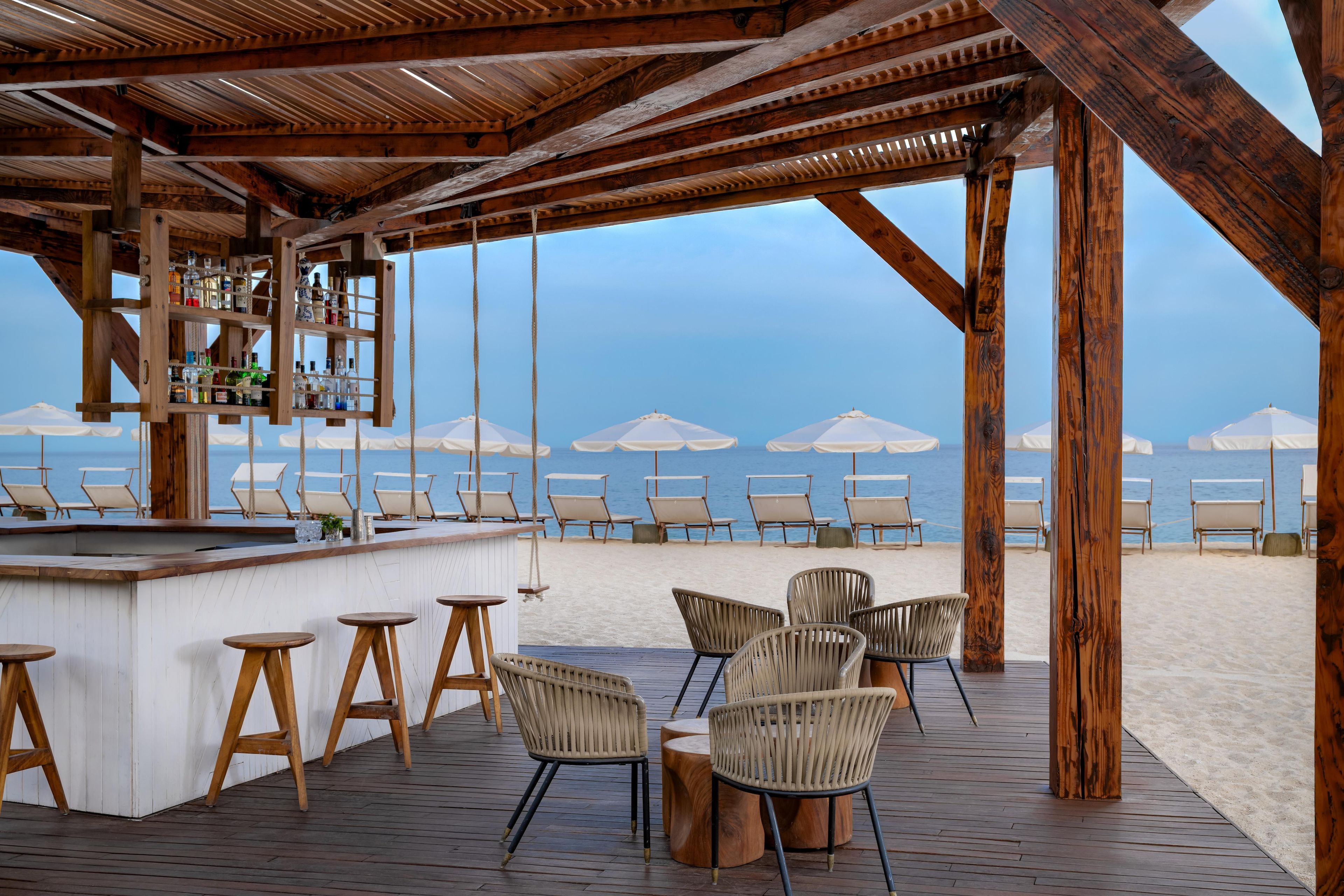 Un bar en la playa con muebles de madera y vistas al mar.