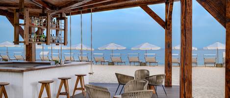Un bar en la playa con muebles de madera y vistas al mar.