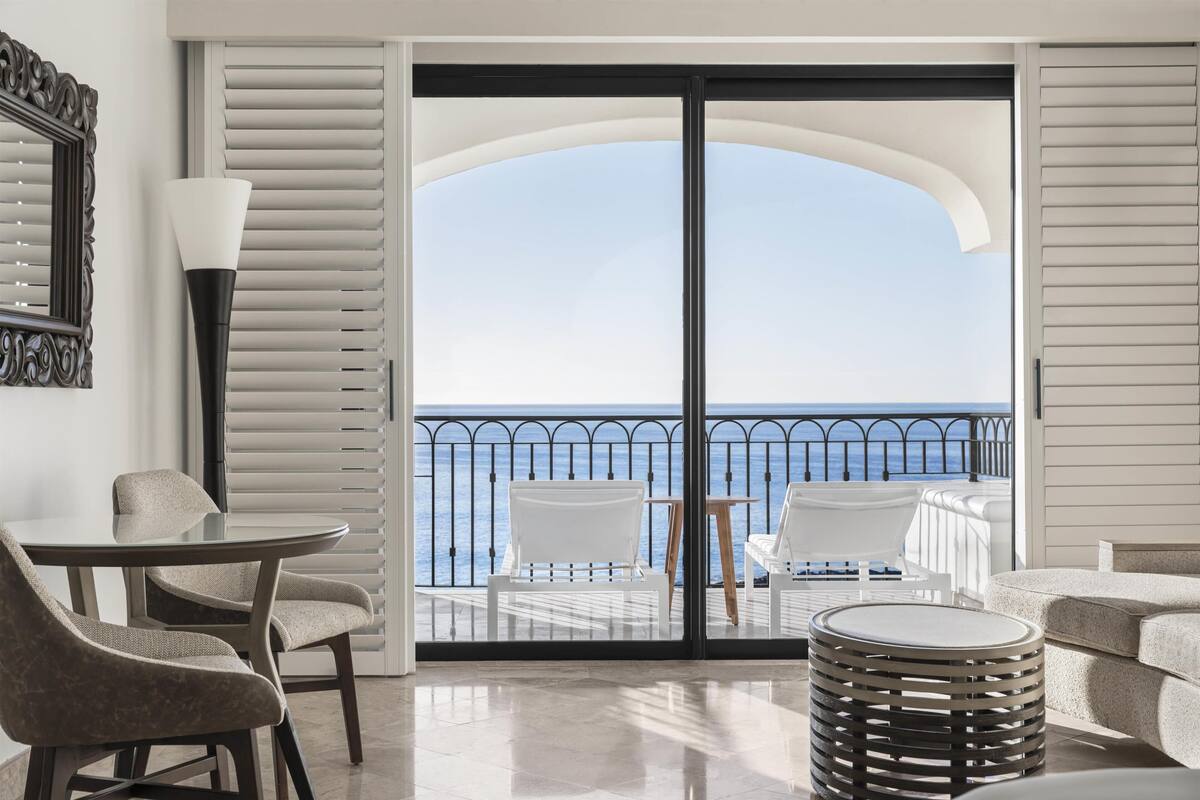 A balcony with a view of the sea, a table with chairs, and a lamp.