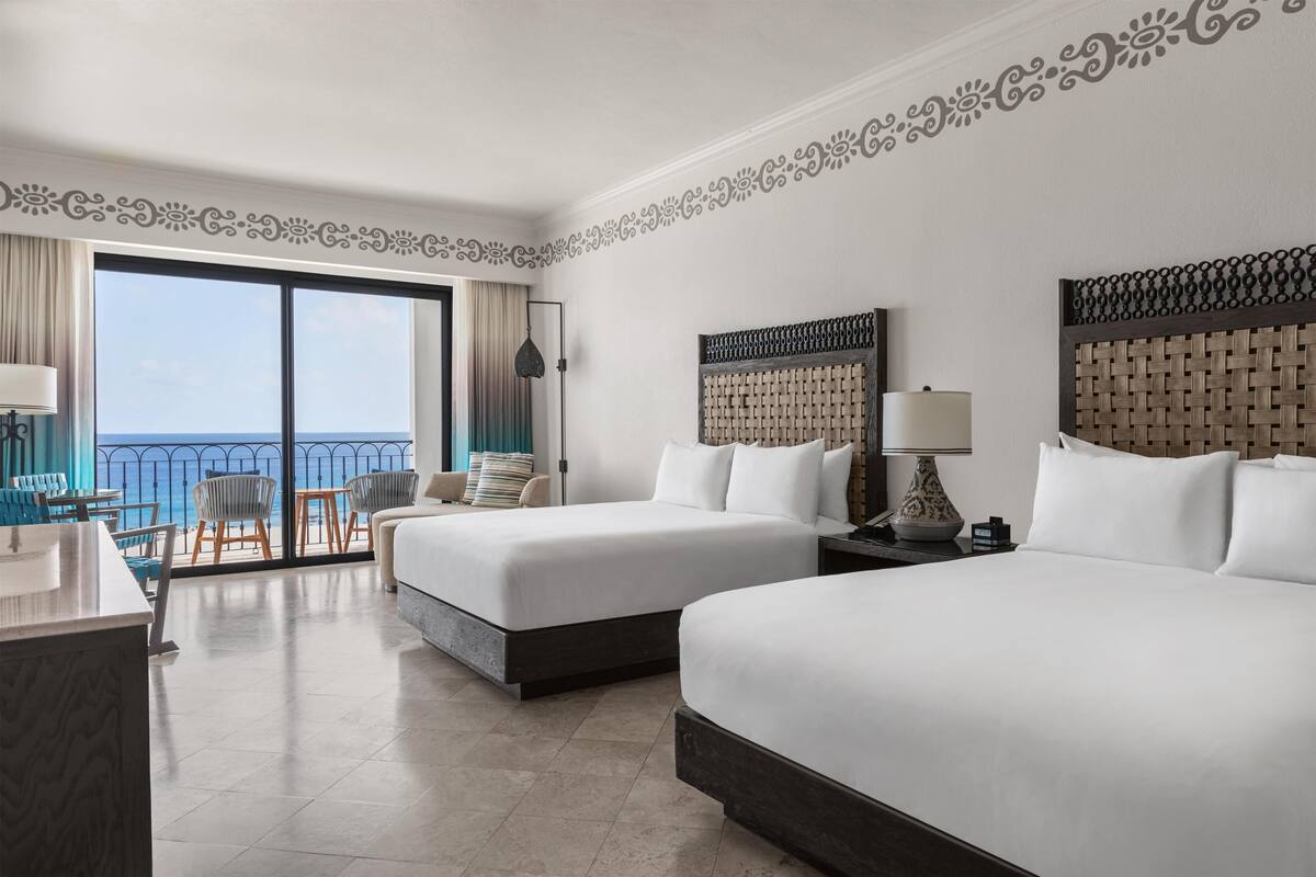 A hotel room with two beds, a balcony with a view, and a desk with a chair.