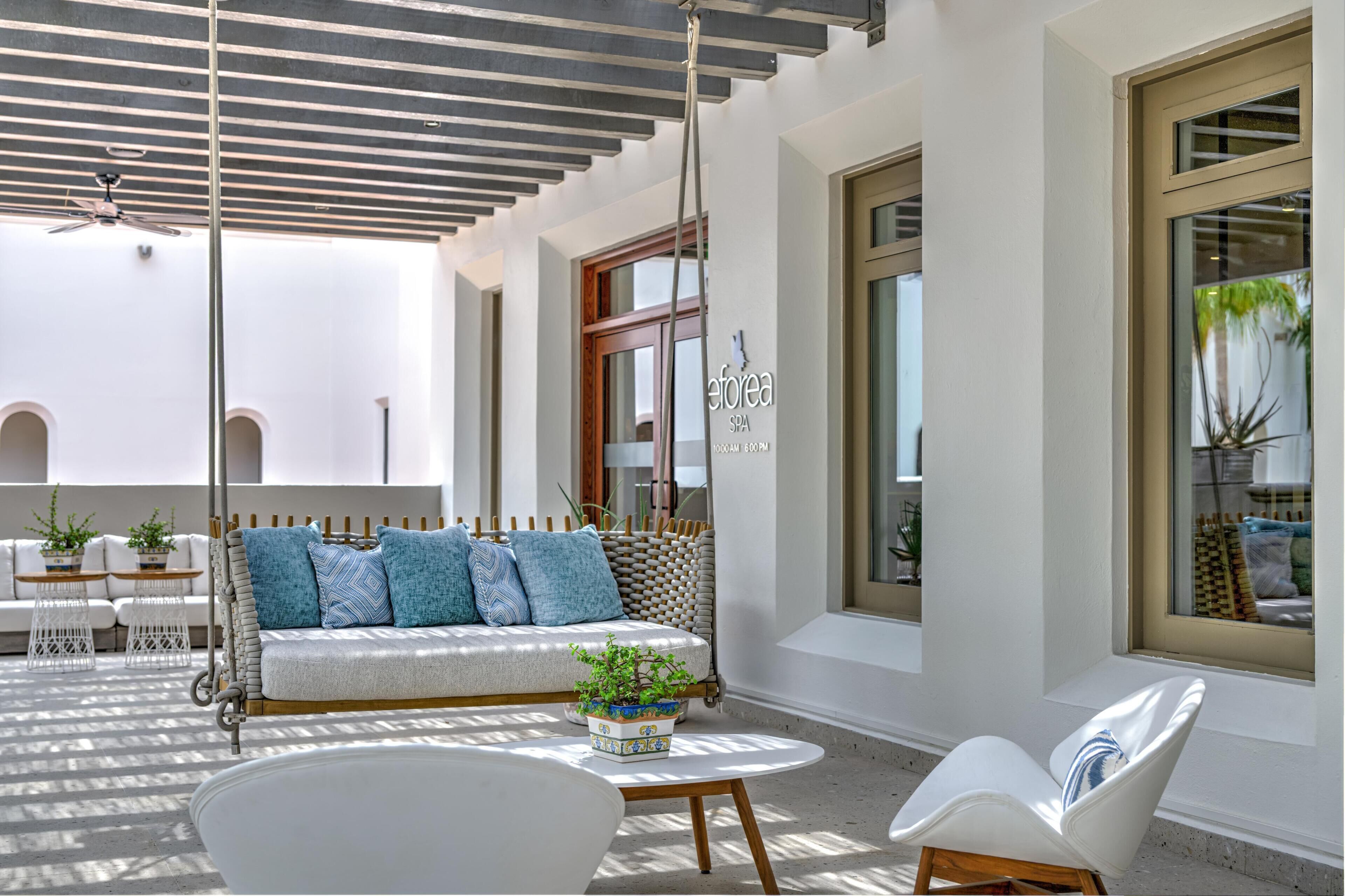 A spa area with a white sofa, a white chair, a round table, and a ceiling fan.
