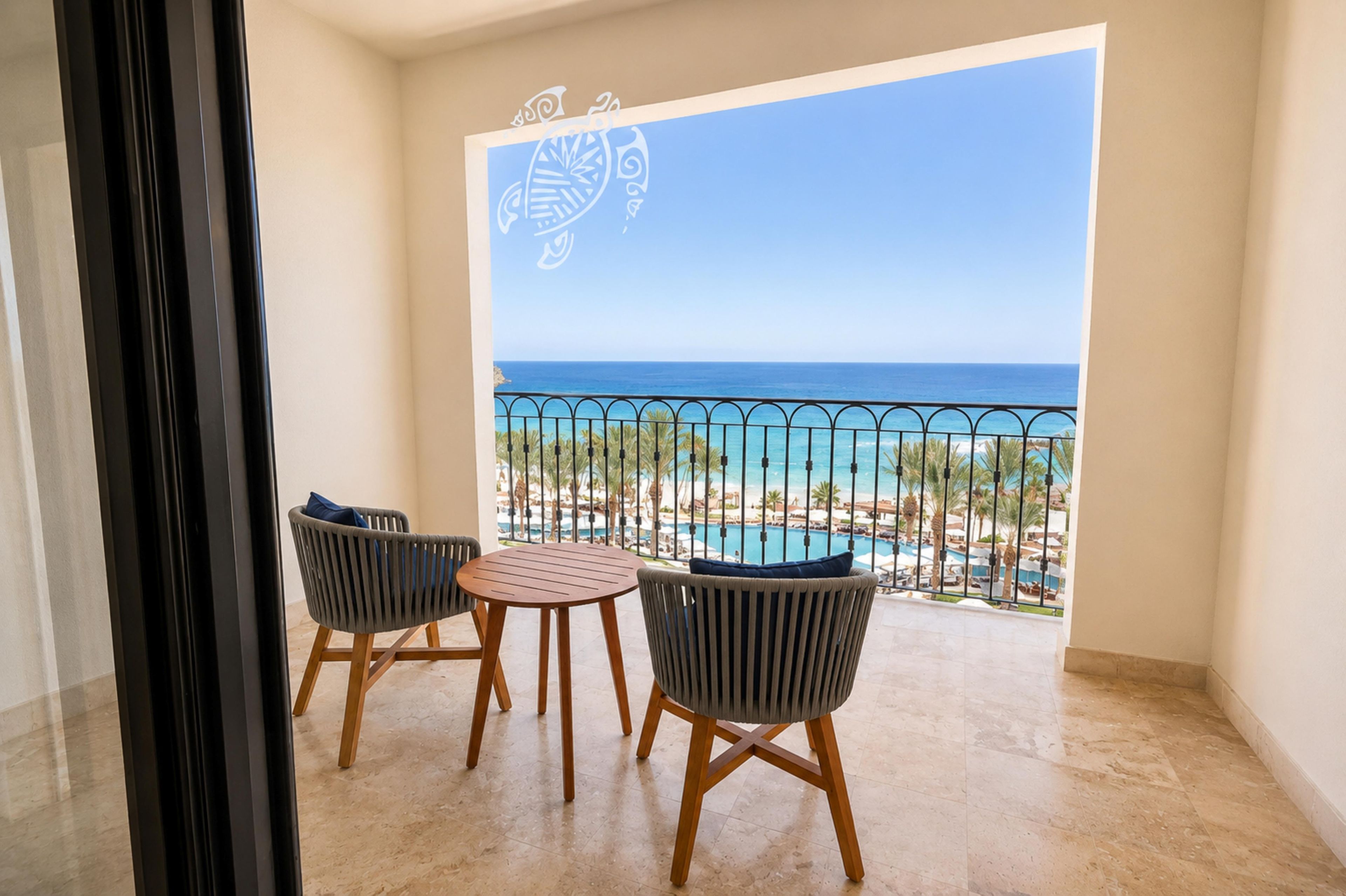 A balcony with a view of the ocean, two wicker chairs, and a small round table.