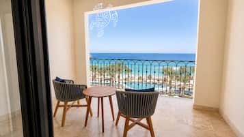 A balcony with a view of the ocean, two wicker chairs, and a small round table.