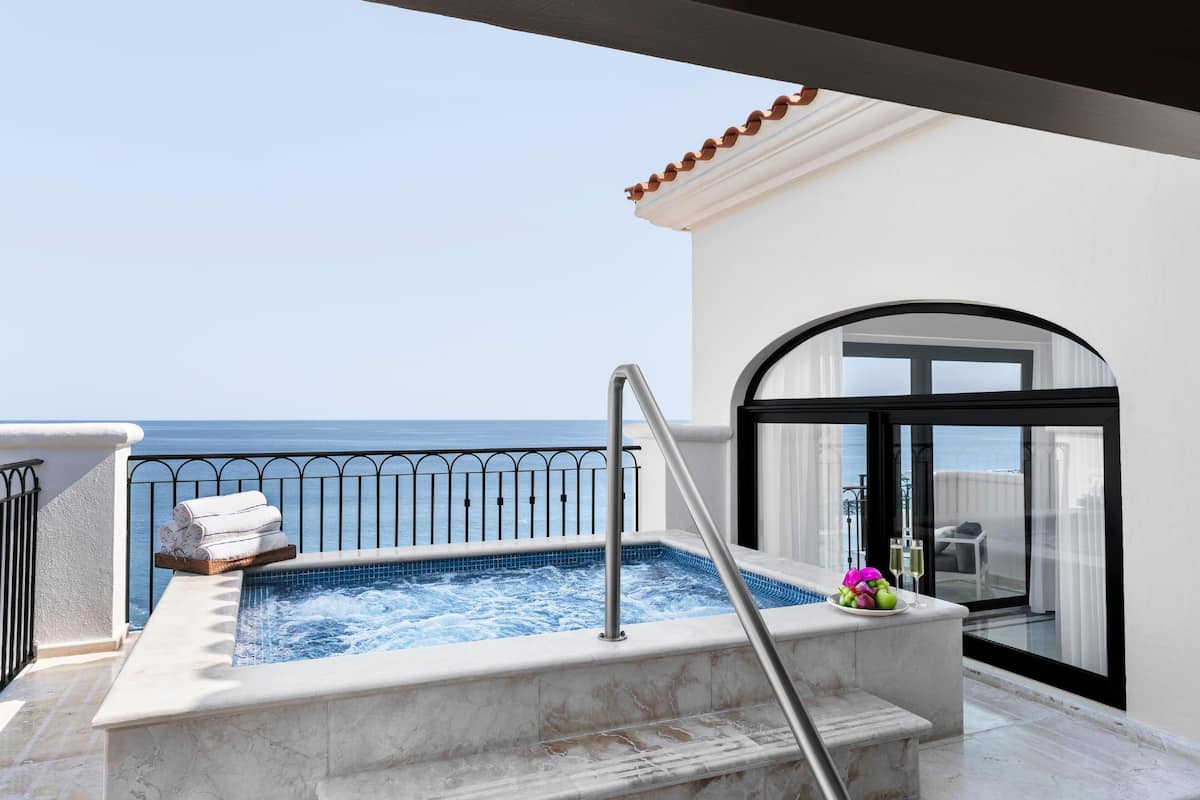A balcony with a hot tub, a view of the sea, and a door leading to a room.