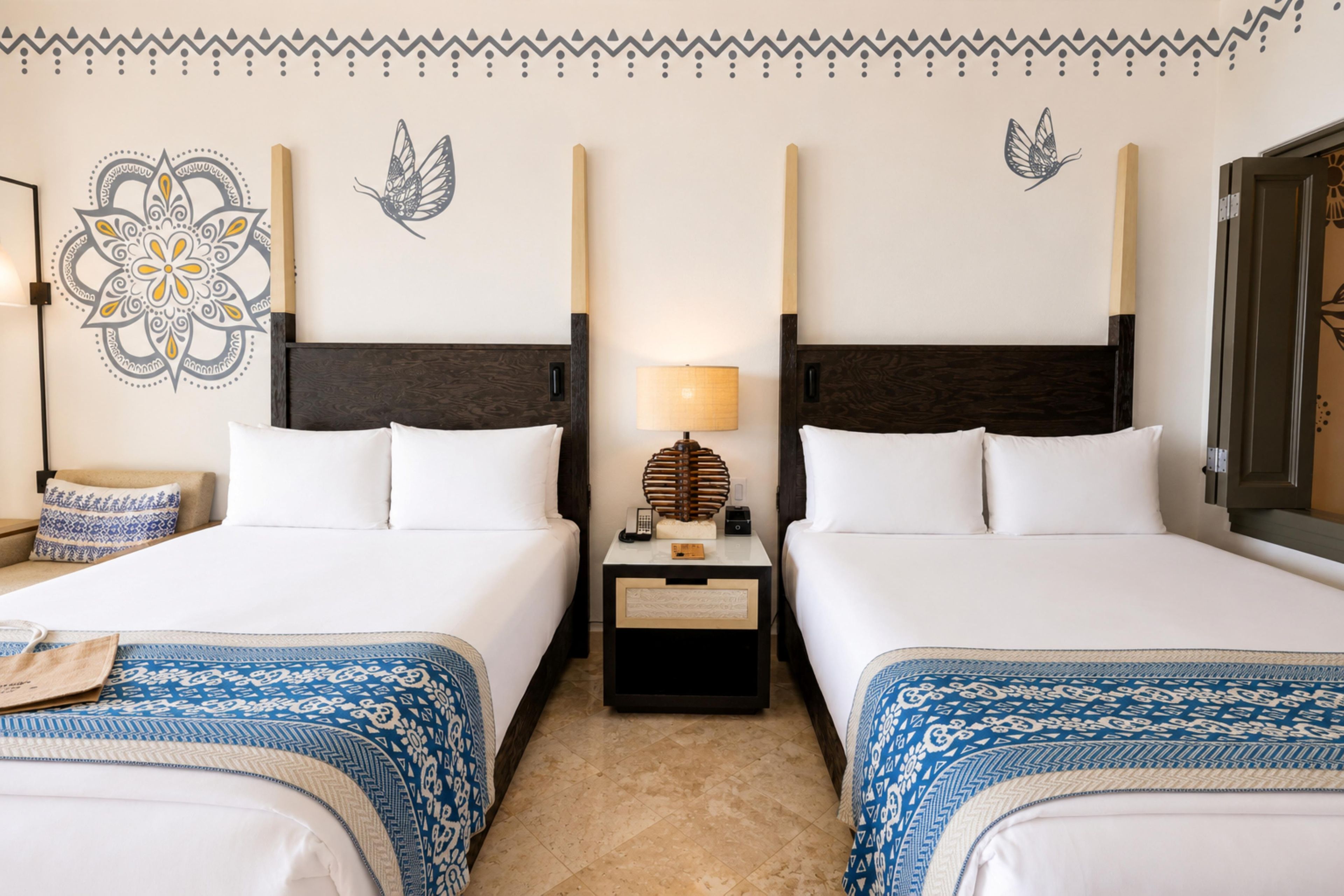 A hotel room with two beds, a nightstand with a lamp, and decorative wall art.