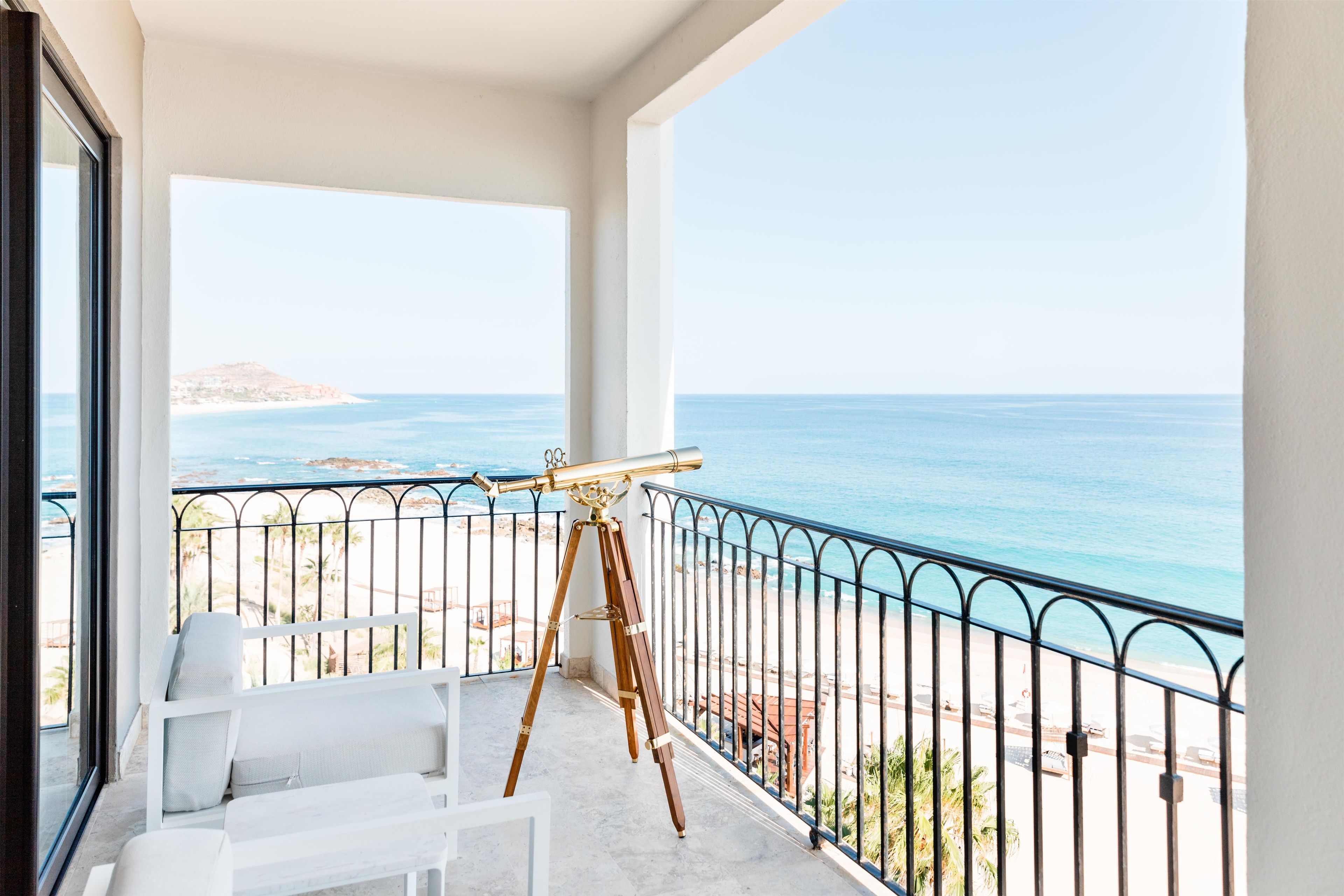 A balcony with a telescope, white furniture, and a view of the sea.