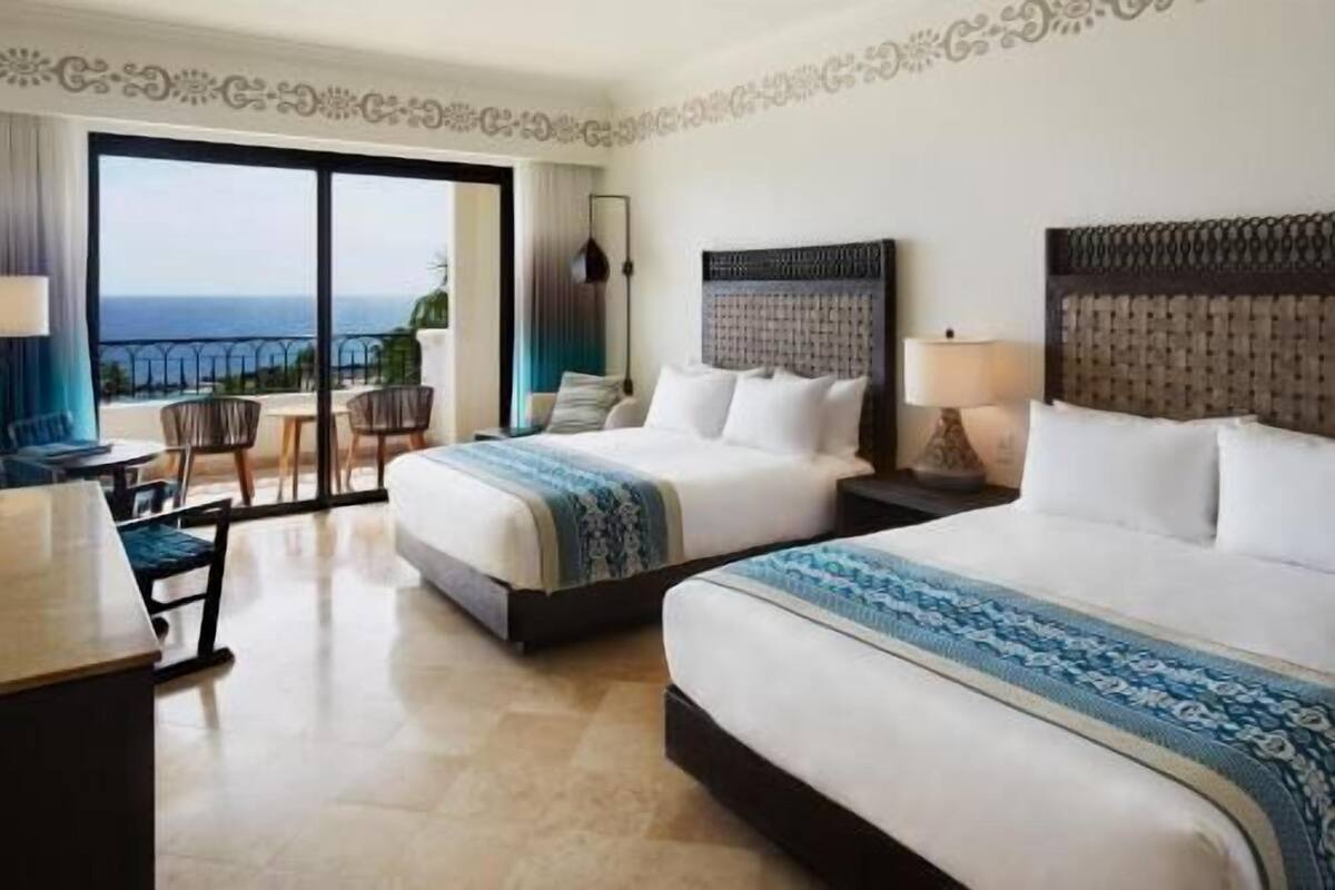 A hotel room with two beds, a balcony with a view, and a dining area.