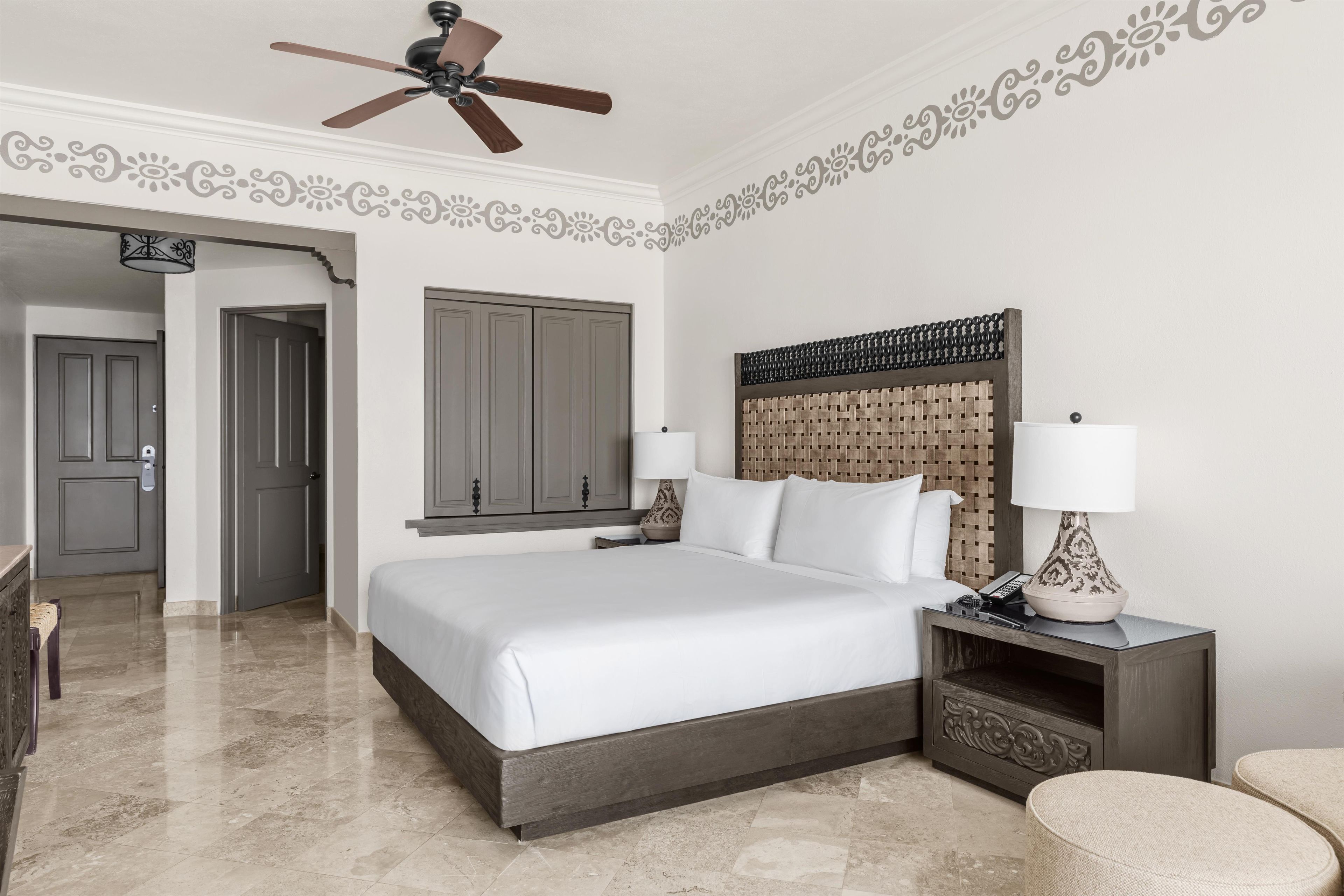 A hotel room with a bed, nightstands, a lamp, a ceiling fan, and a decorative wall.