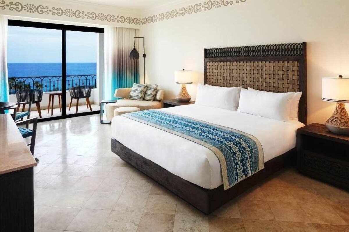 A hotel room with a large bed, a balcony with chairs, and a view of the ocean.