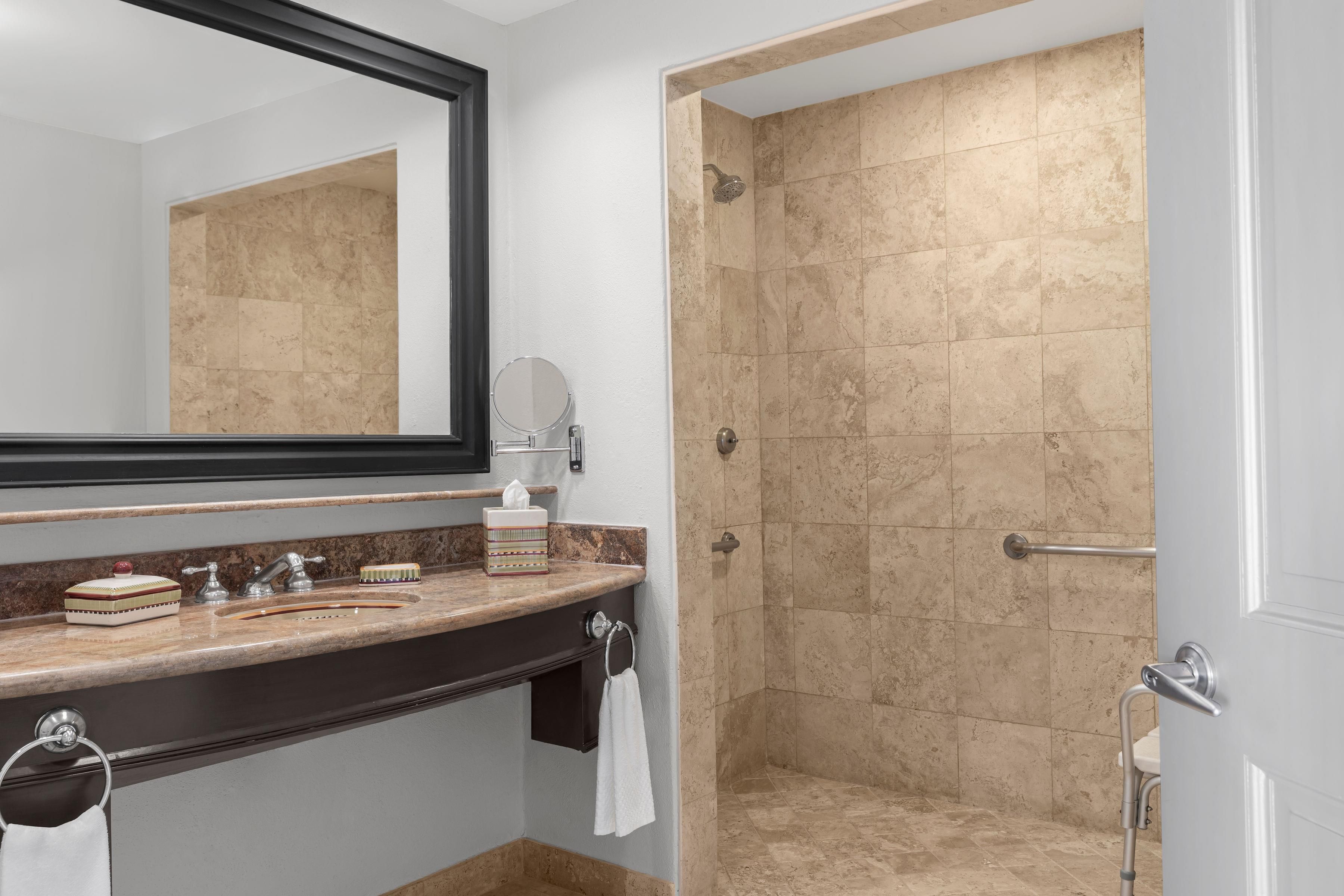 Een badkamer met een marmeren aanrechtblad, een spiegel, een handdoekhouder en een douchegedeelte met beige tegels.