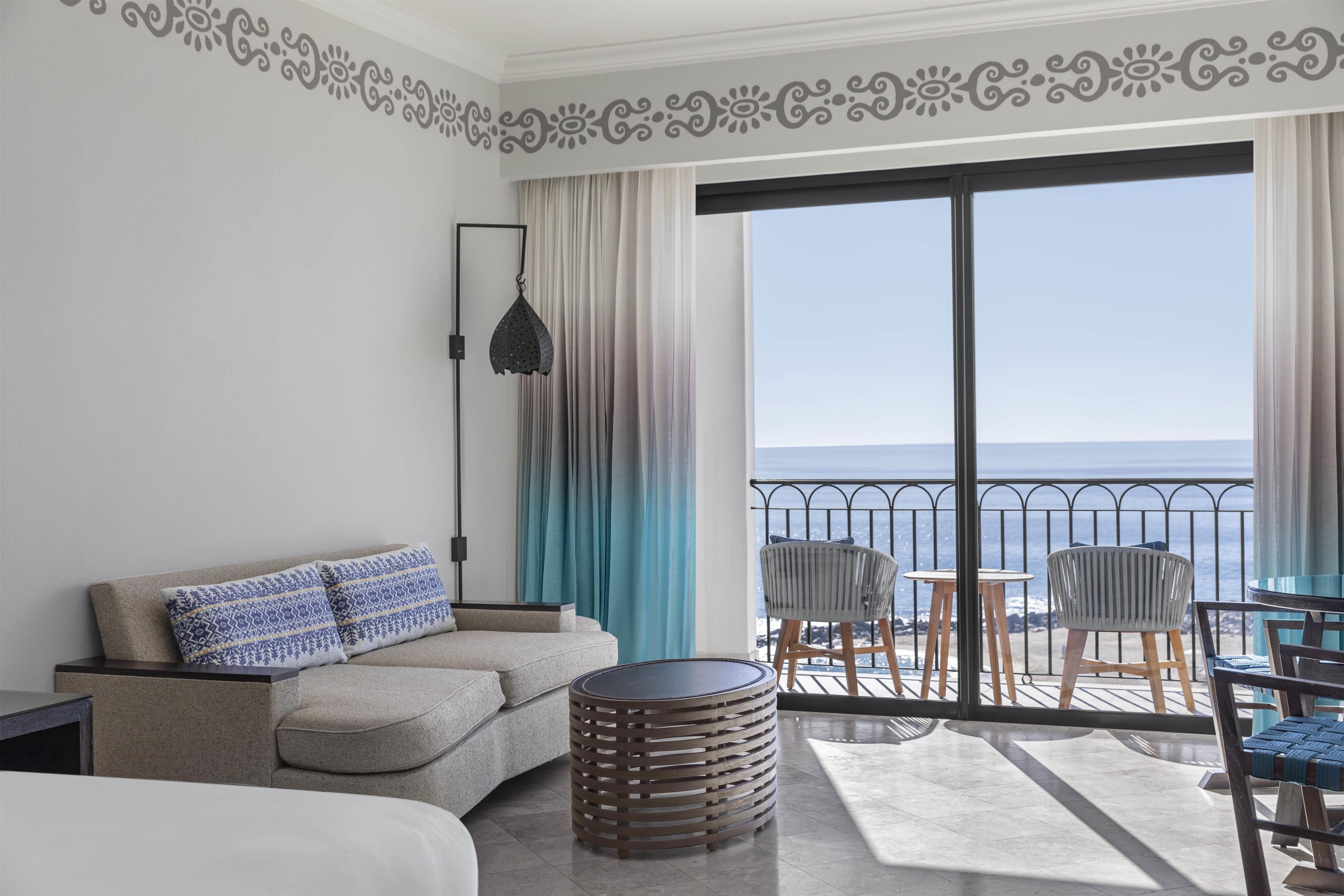 A hotel room with a balcony, a sofa, a round table, and a view of the sea.