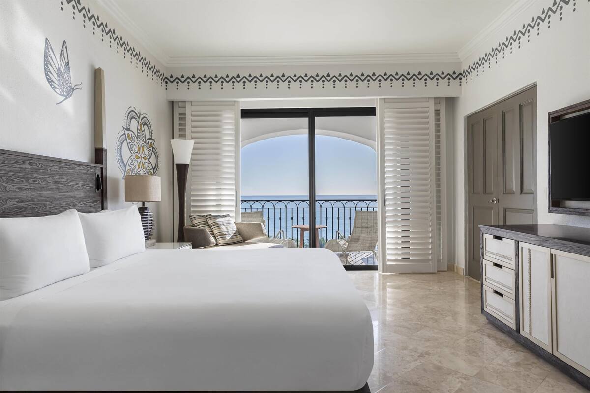 A hotel room with a large bed, a TV, a balcony with a view, and decorative wall art.